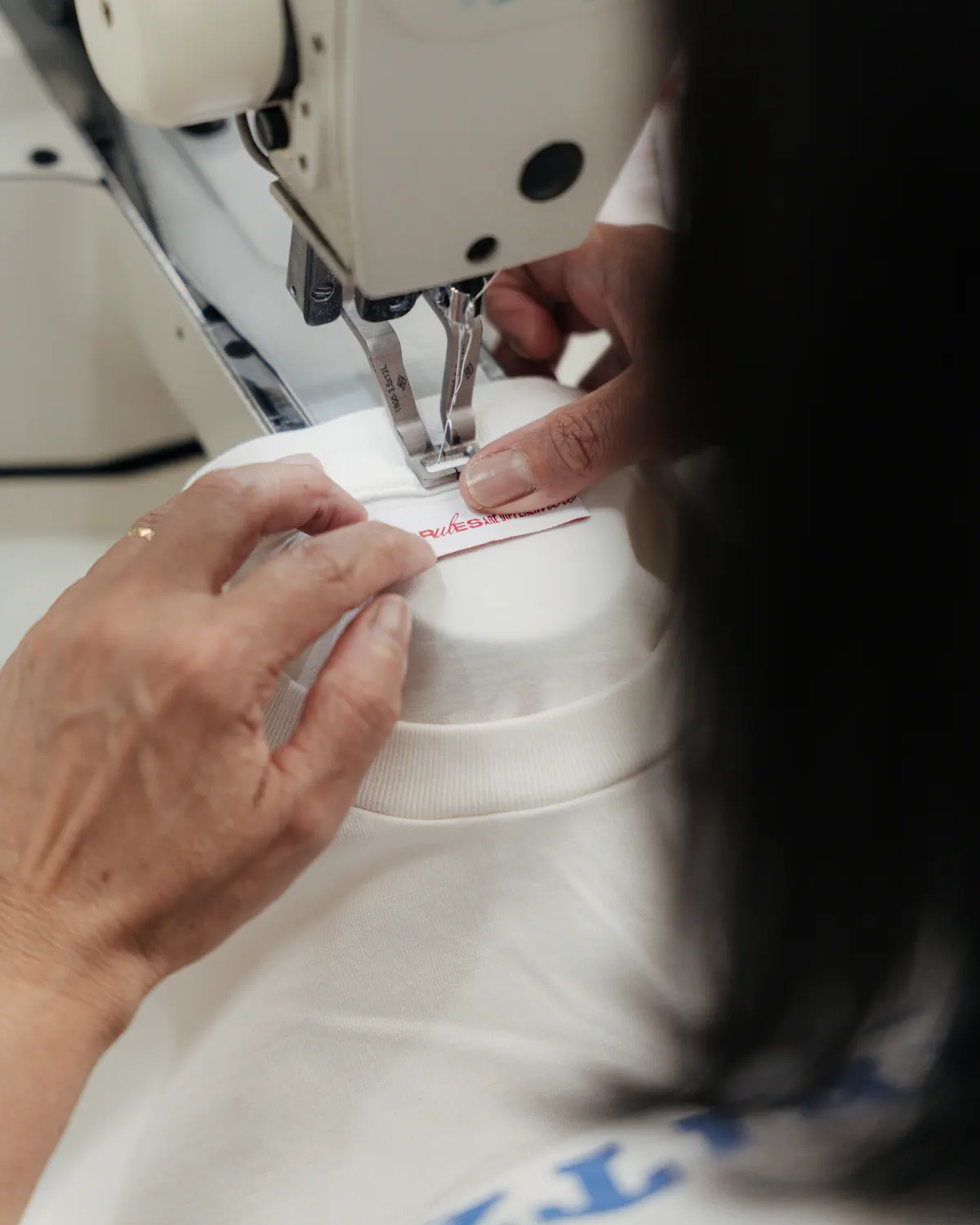 Woven label being sewn into the neck of a white T-shirt at a sewing machine