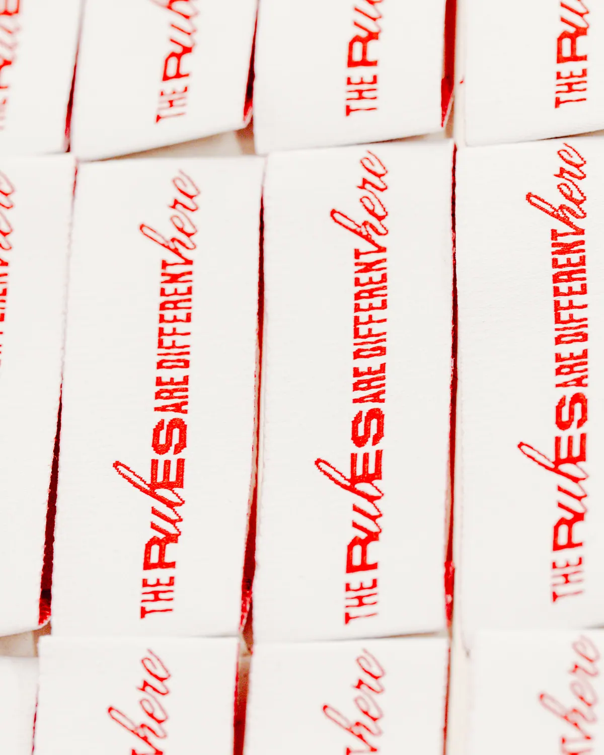 Stack of red and white woven labels reading The rules are different here
