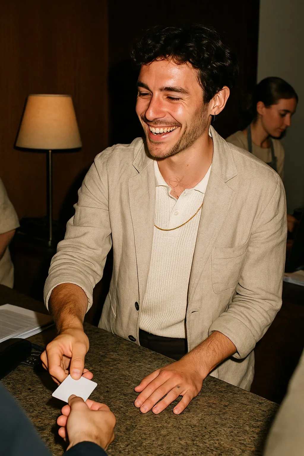 AI concept: a hotel front desk host laughing softly while sliding a key card across a stone counter, in a cream knitted polo under a soft oatmeal linen jacket