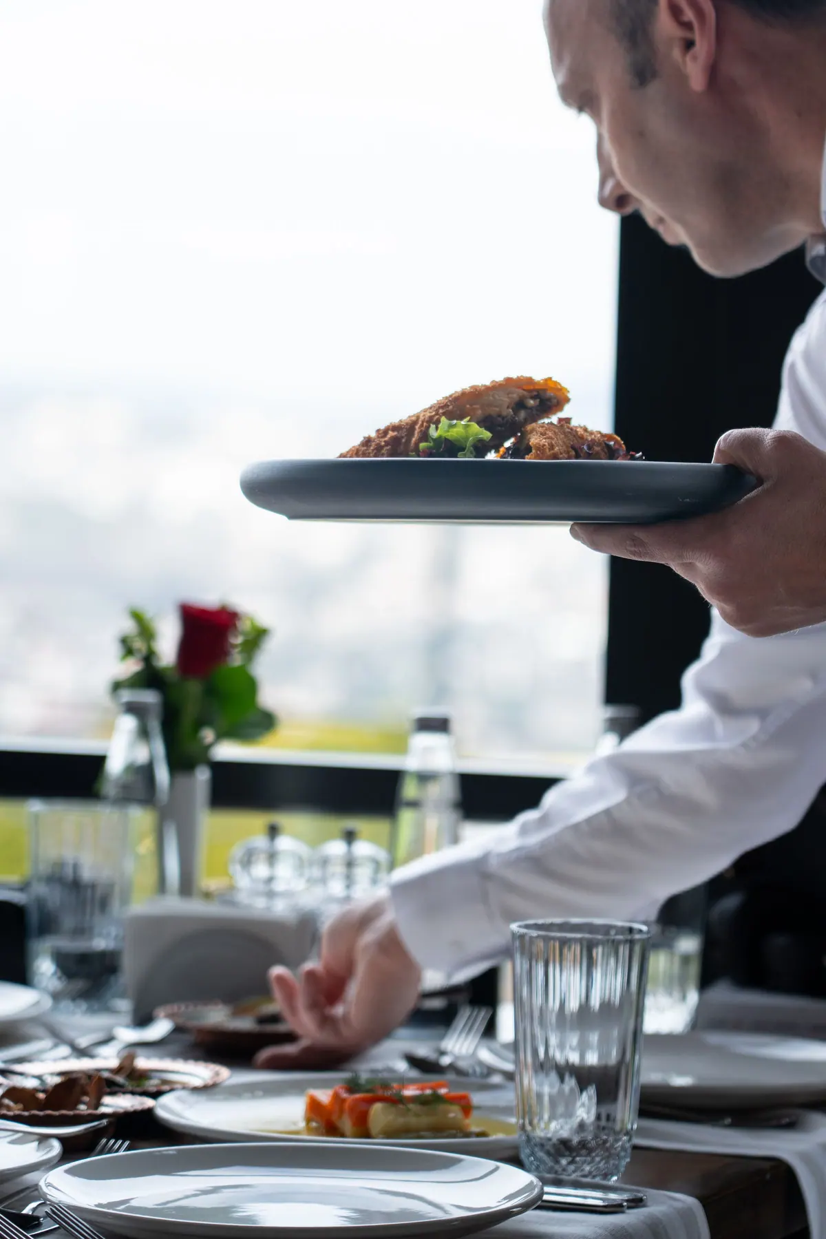 Venue waiter carrying a plated dish to a laid table by a window
