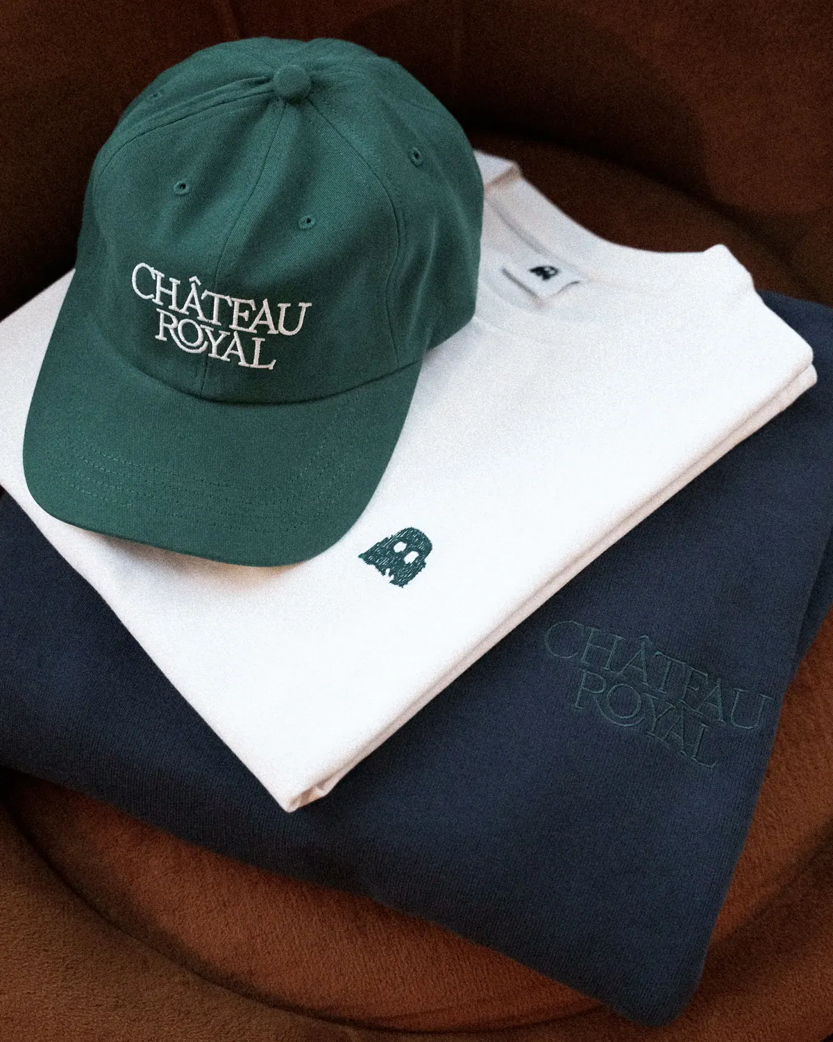 Château Royal green cap on a folded white T-shirt and navy sweatshirt