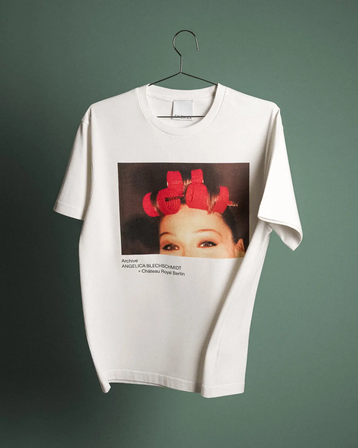 Château Royal white T-shirt with a printed photograph, on a hanger against green