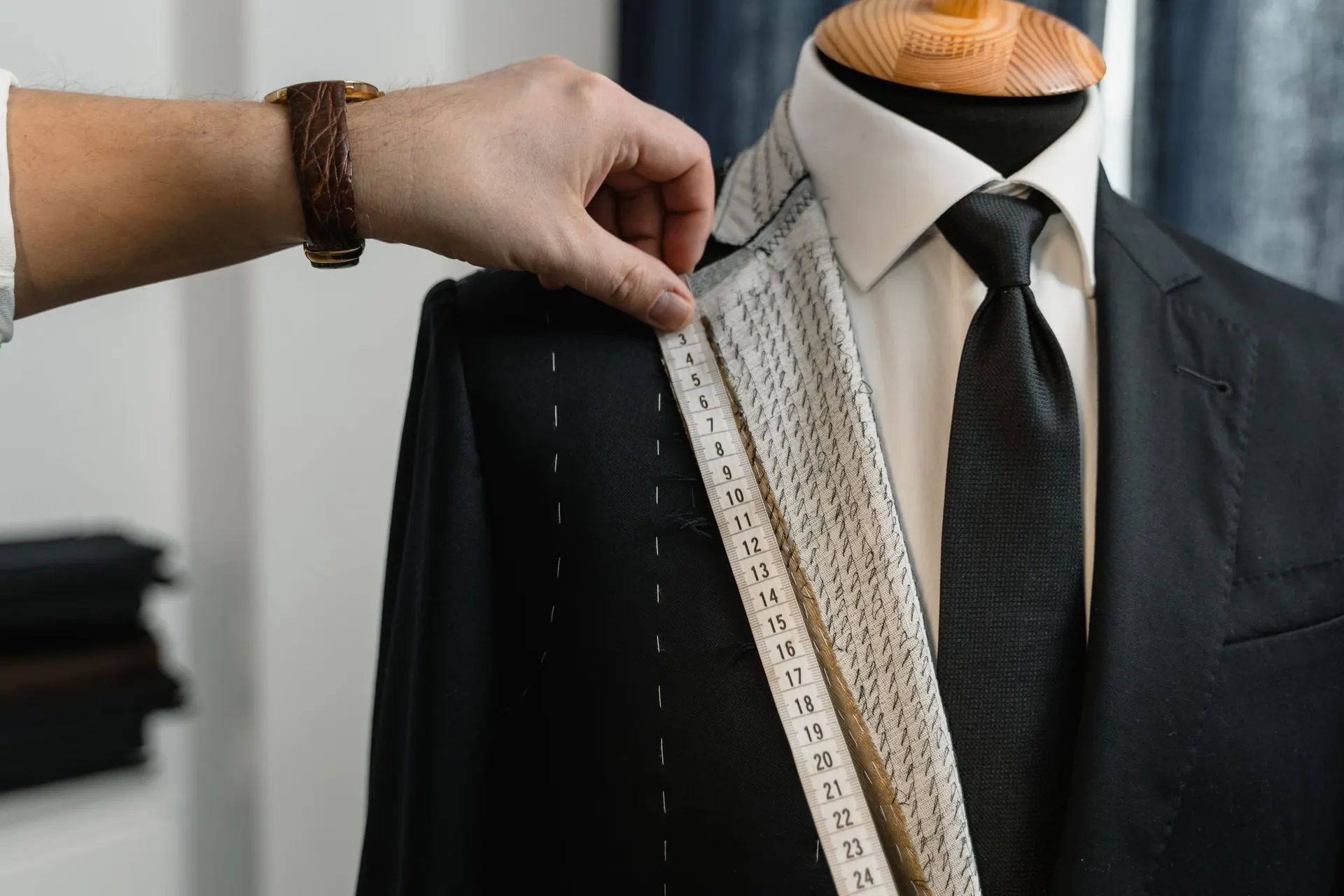 Tailor measuring the chalk-marked lapel of a dark jacket on a mannequin