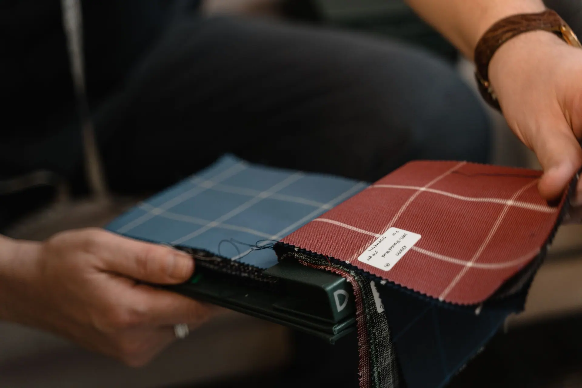 Hands with wool suiting swatches in blue, red and check on a workbench