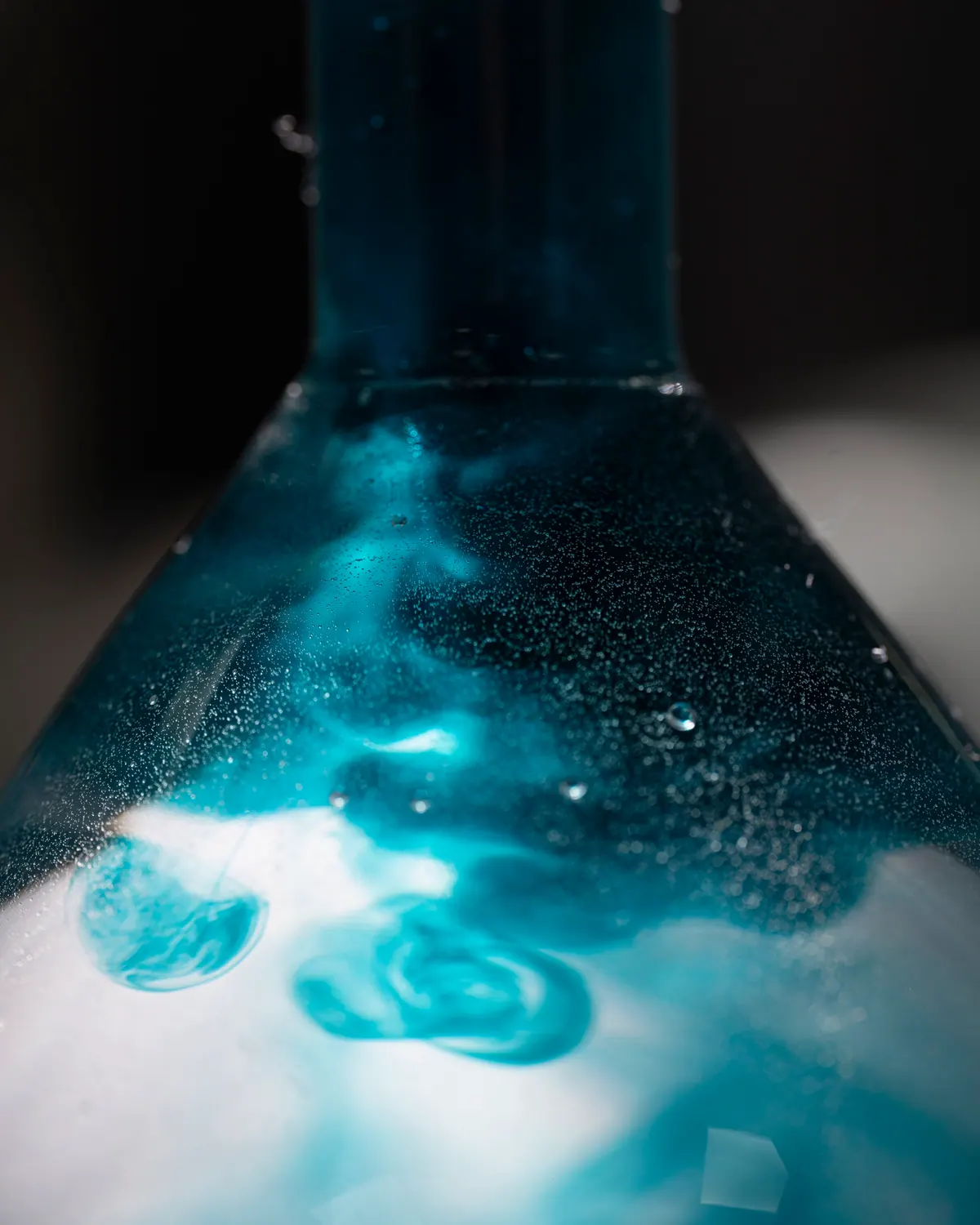 Close-up of teal dye developing and foaming inside a glass lab flask