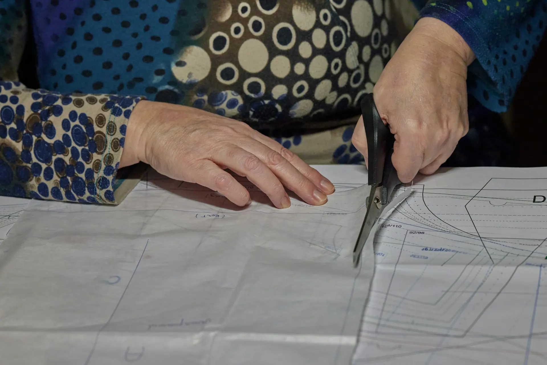 Hands cutting paper pattern pieces with shears on a cutting table