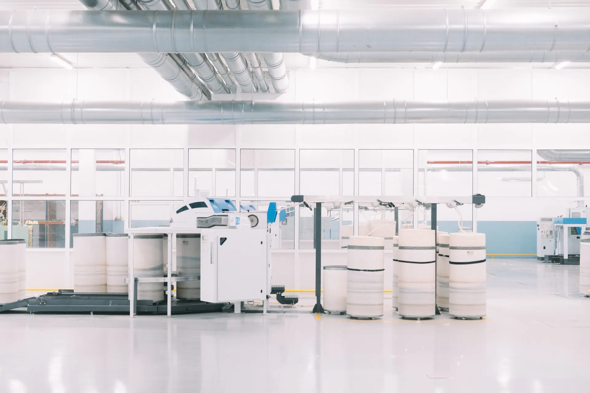 A production floor with overhead ducting and rows of wound yarn cones