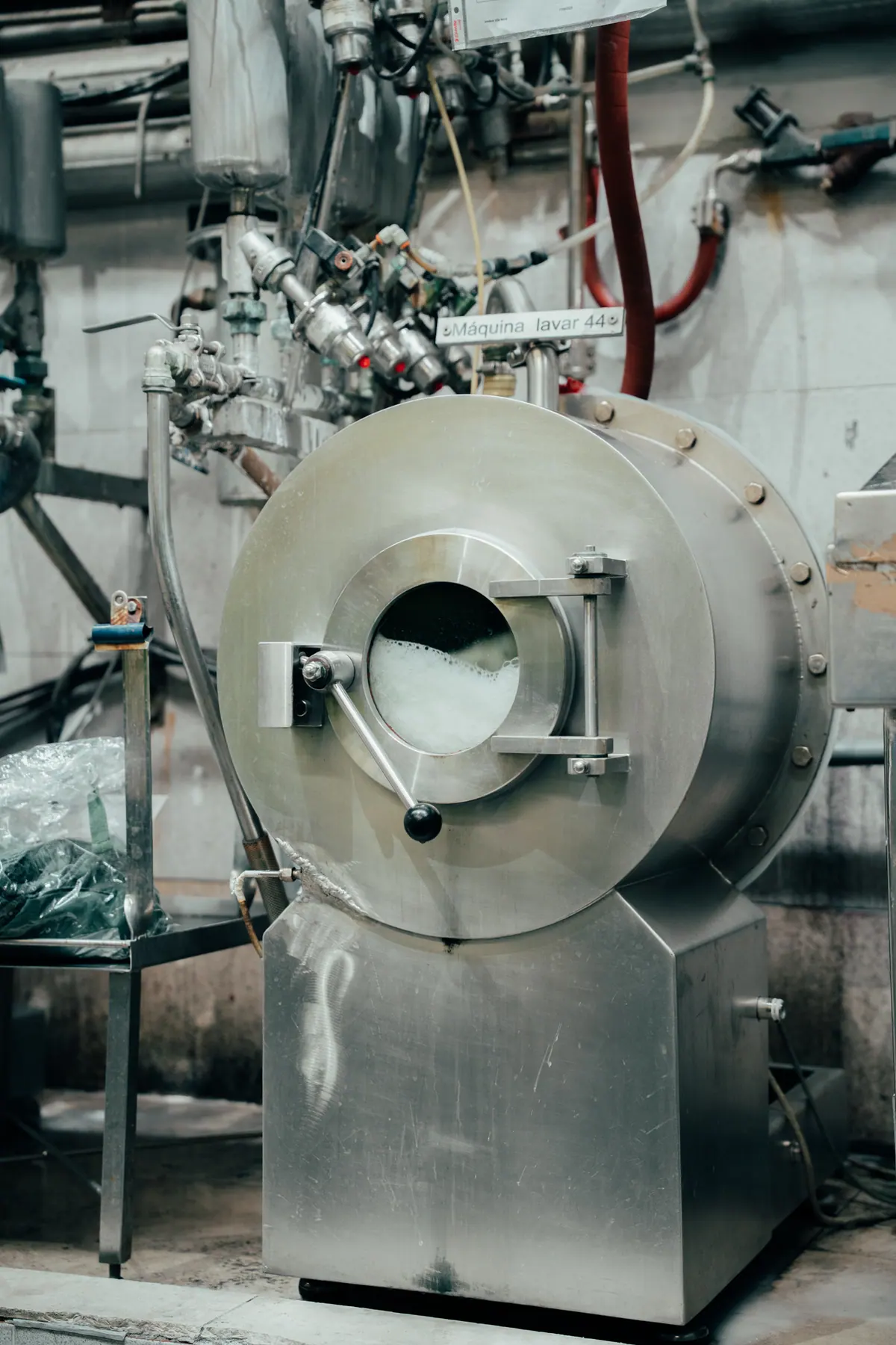 A garment-washing machine on a factory floor in Portugal, drum door open with foam visible inside