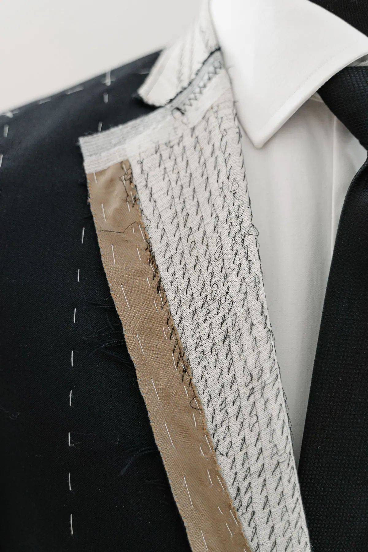 Unfinished jacket lapel with exposed canvas and basting stitches over a shirt collar