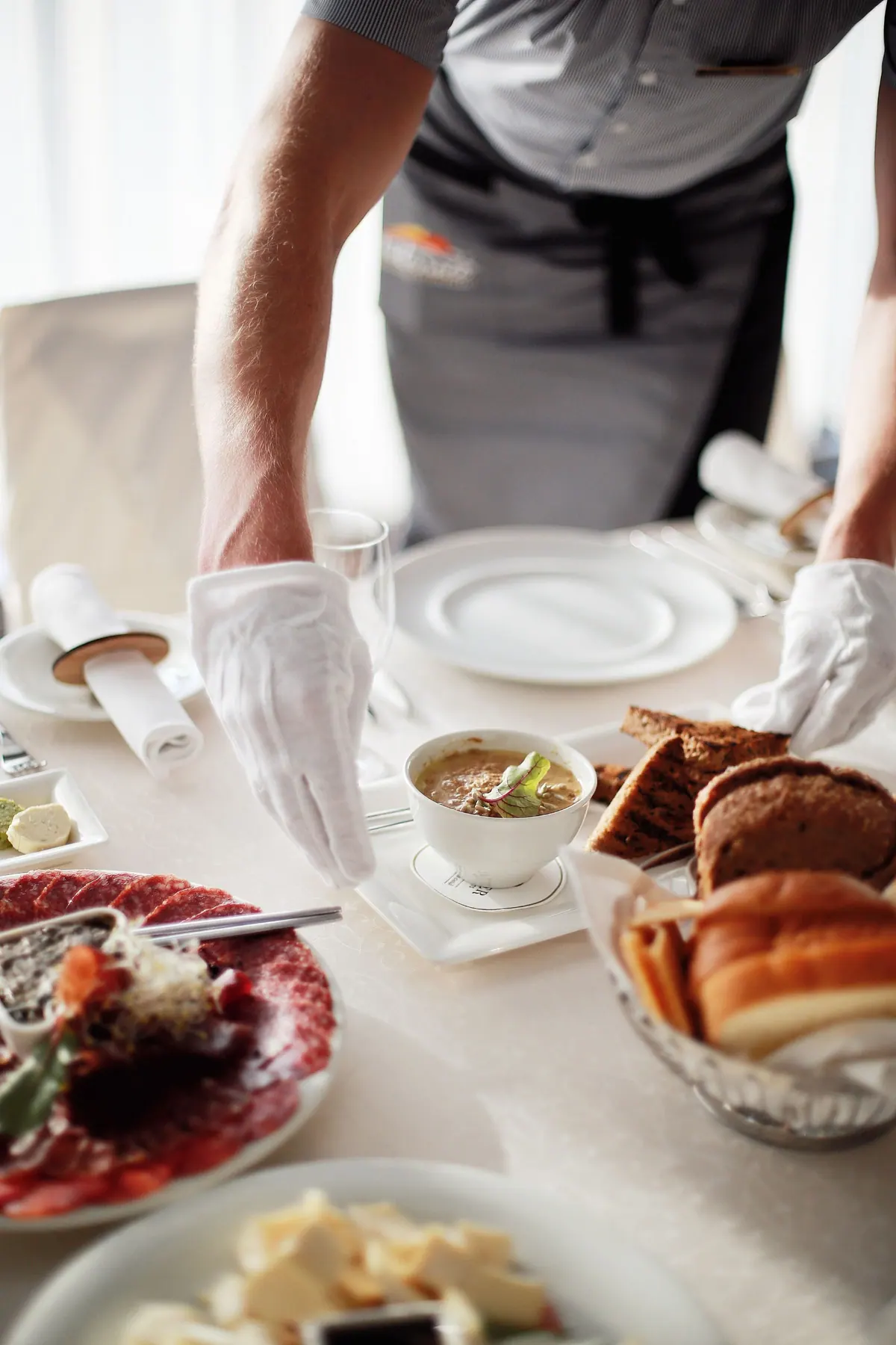 Gloved hands of a waiter placing plates on a set table