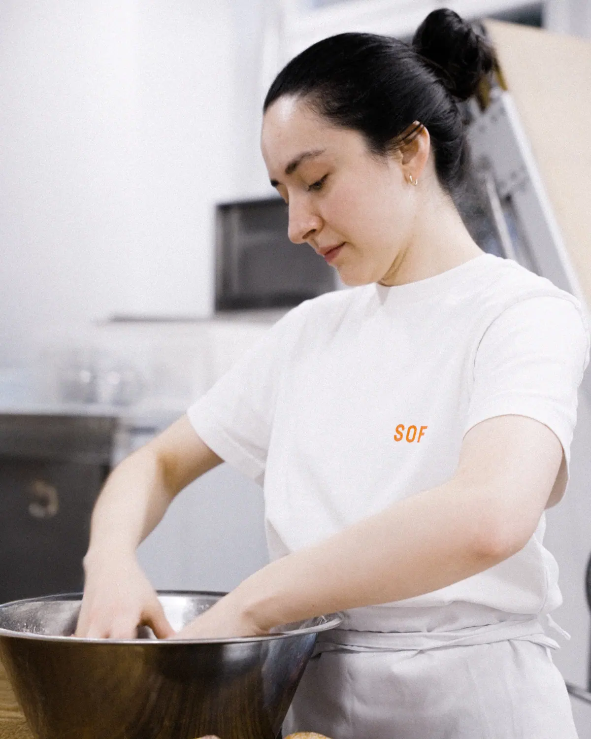 Sofi Bakery team member in a white SOFI T-shirt and apron shaping dough