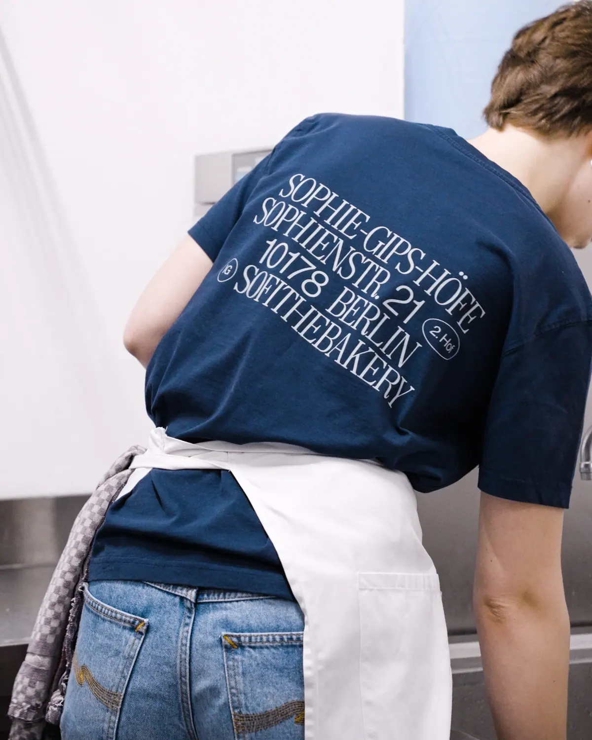 Sofi Bakery team member in a navy T-shirt with the address print on the back