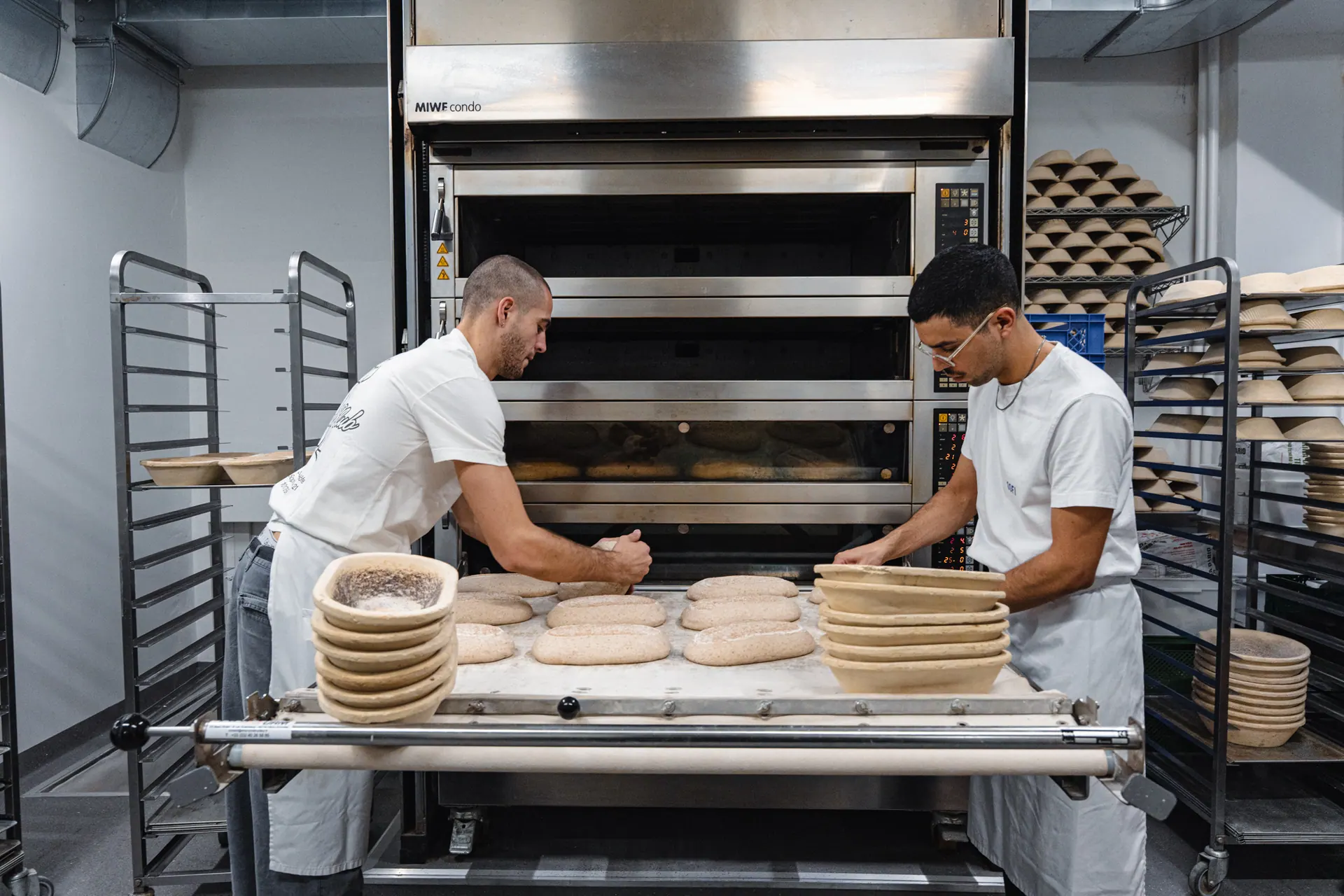 Two Sofi Bakery bakers in white T-shirts and aprons at the oven racks