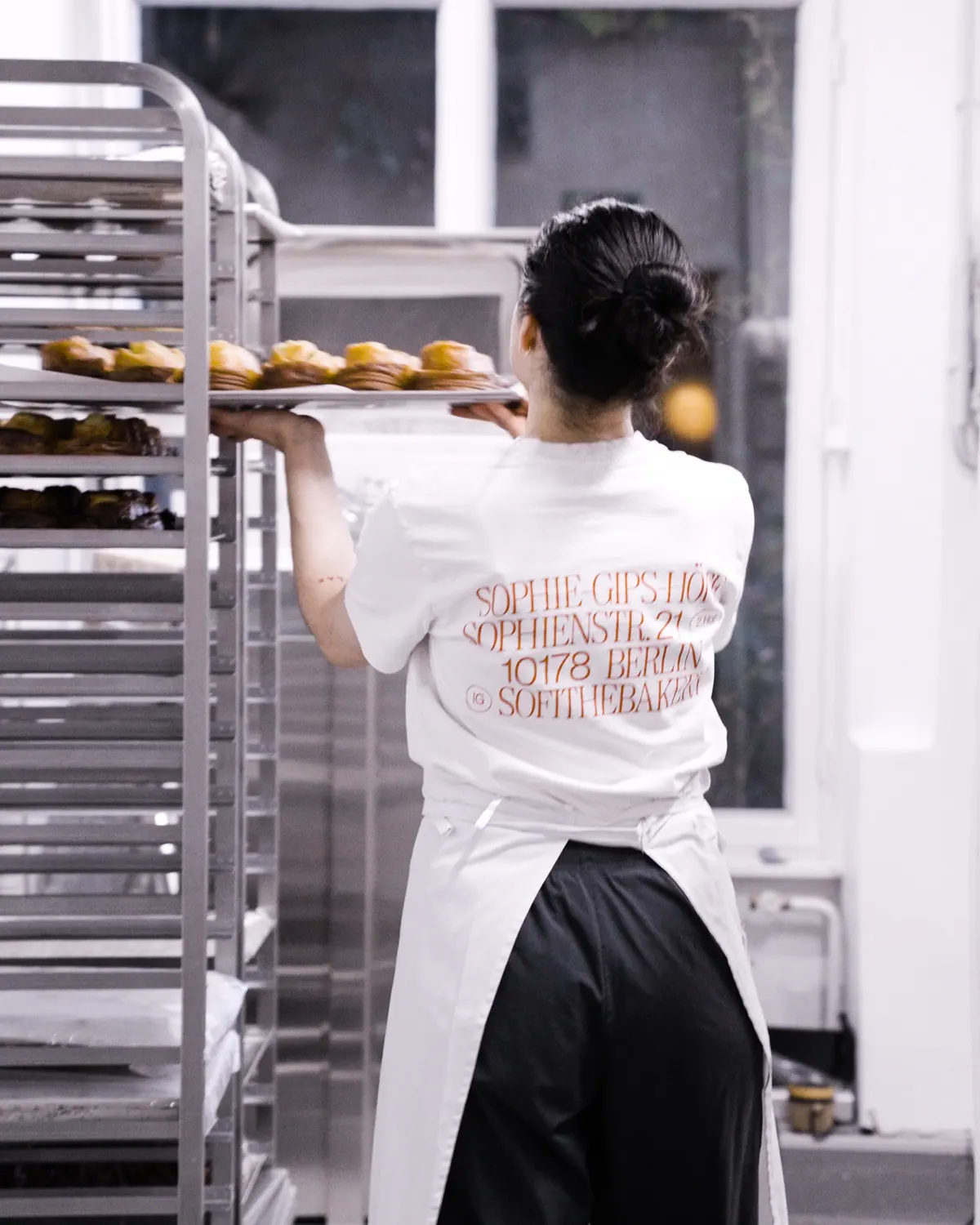 Sofi Bakery team member in apron carrying a tray of pastries past the ovens