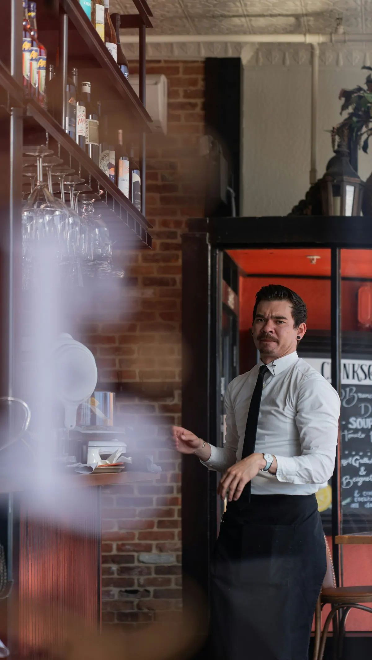 Bartender in a white shirt and black apron behind a bar
