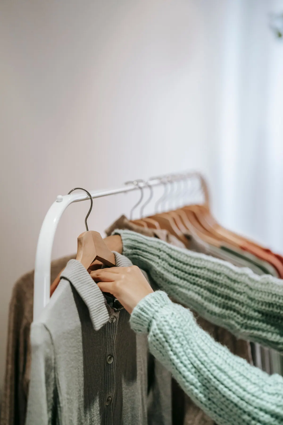 Hands lifting a grey garment on a wooden hanger from a white rail